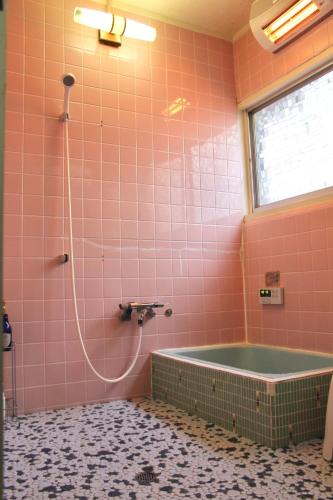 baño alicatado de color rosa con bañera y ventana en Guest House Toranjyo-lit, en Tamano