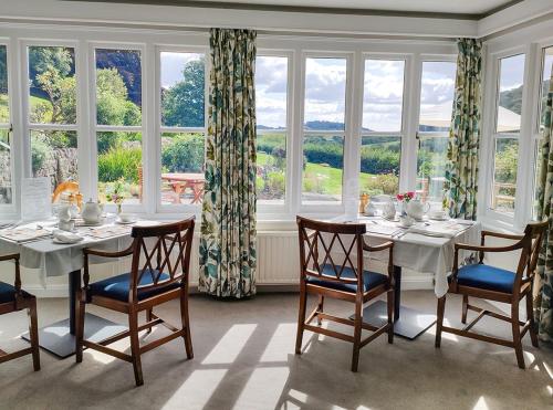 a dining room with a table and chairs and windows at Eastwrey Barton Country House in Lustleigh