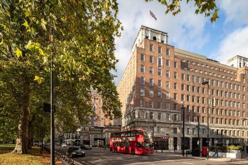 a red double decker bus driving down a city street at Grosvenor House Suites in London
