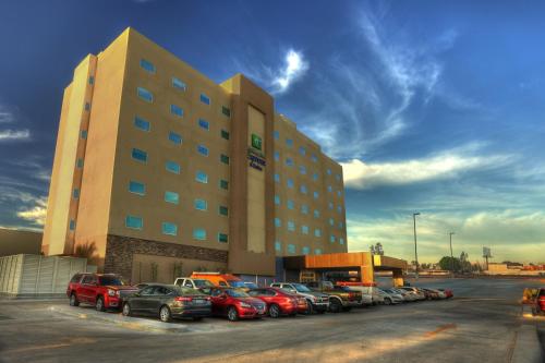un grand bâtiment avec des voitures garées dans un parking dans l'établissement Holiday Inn Express & Suites Mexicali, an IHG Hotel, à Mexicali