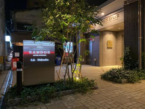 a sign in front of a building with a tree at Randor Hotel Fukuoka in Fukuoka