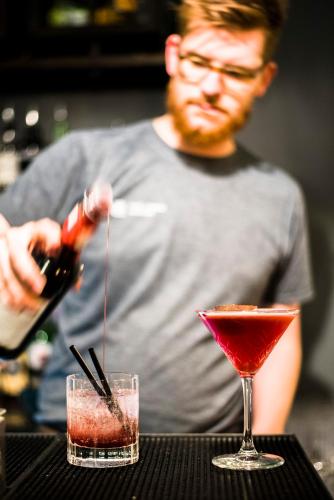 a man is pouring a red drink into two cocktails at The Lodge Duxford in Duxford
