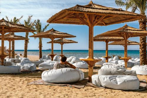 a man sitting on a beach with pillows and umbrellas at Robinson Soma Bay in Hurghada