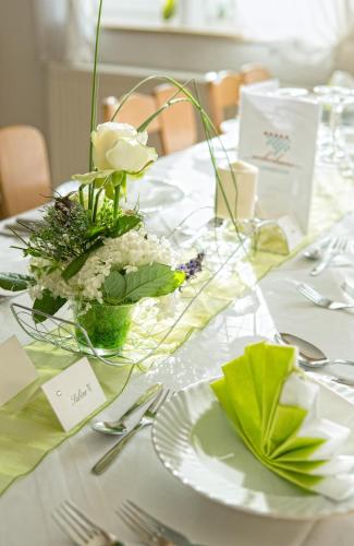 a table with white plates and a vase of flowers at Landgasthof Weberhans in Harburg