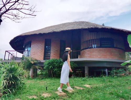 a woman in a hat walking in front of a building at Tomodachi Retreat - Làng Mít in Sơn Tây