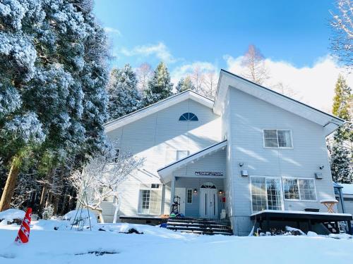 a white house in the snow with trees at Snow Elephant in Hakuba