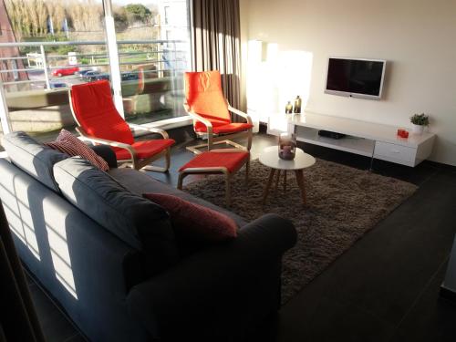 Una sala de estar con un sofá y sillas y un televisor. en Vakantie Appartement Ella, en De Haan