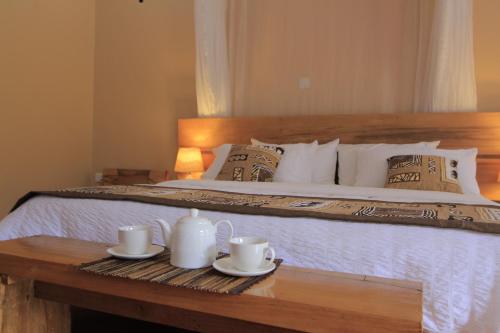 a bedroom with a bed with two cups and a table at Kisubi Forest Cottages in Entebbe