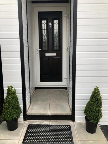 a black door on a white house with two plants at Beechwood Garden Suite in Newtownabbey