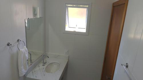 a white bathroom with a sink and a window at Residencial JL Maresias Apartamentos in Maresias