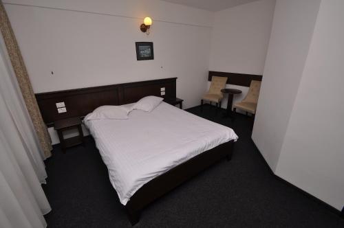 a small bedroom with a white bed and a chair at Hotel Cerbul in Statiunea Borsa