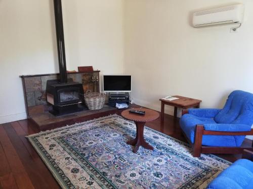 Woodlands of Balingup Bush Cottages في بالينغوب: غرفة معيشة مع كرسي ازرق وطاولة ومدفأة
