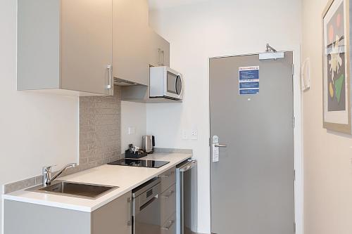 a white kitchen with a sink and a microwave at Ramada Suites By Wyndham Victoria Street West in Auckland