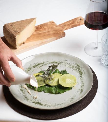 a person pouring cheese onto a plate of food at Hotel Rovanada Wellness & BergNatur in Vals