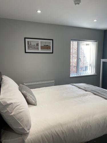 a bedroom with a bed with white sheets and a window at Brownlows Inn Rooms formerly Riley's Rooms in Liverpool