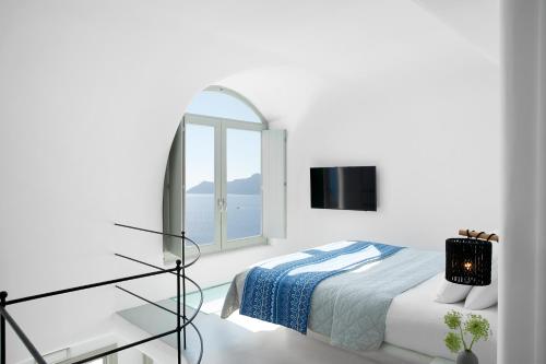 Habitación blanca con cama y espejo en La Perla Villas and Suites - Adults Only en Oia