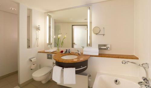 a bathroom with a sink and a toilet and a mirror at Dorint An der Kongresshalle Augsburg in Augsburg