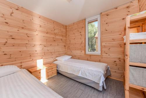 two beds in a room with wooden walls at Drevernos kempingas in Dreverna