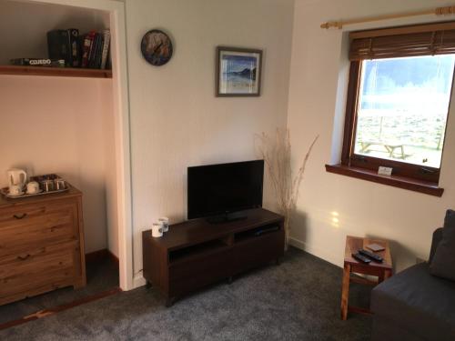 a living room with a flat screen tv on a wooden cabinet at Highland Croft B&B in Onich