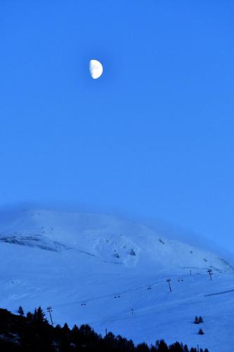 a full moon rising over a snow covered mountain at petite maison à Huez in LʼHuez
