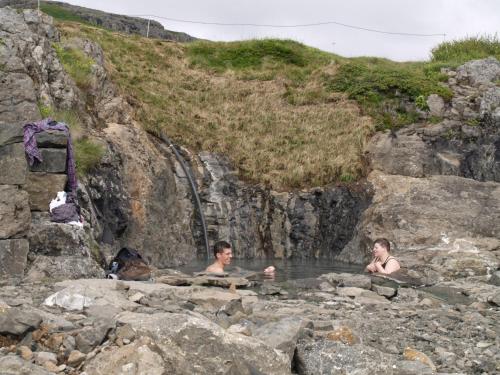 two people swimming in a pool of water next to a waterfall at Hótel Flókalundur in Brjánslækur