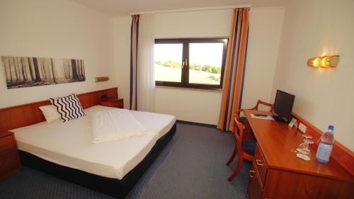 a bedroom with a bed and a desk with a computer at gut-Hotel Tannenhof in Haiger