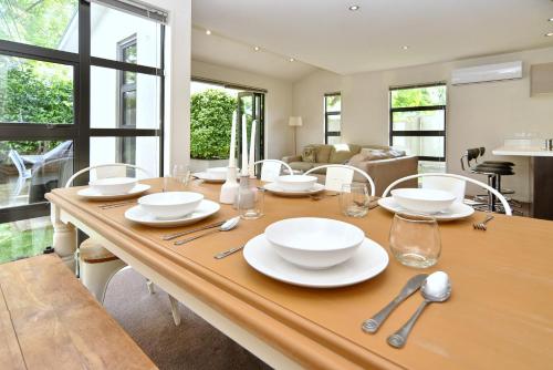 a wooden table with white plates and silverware on it at Hagley Apartment - Christchurch Holiday Homes in Christchurch