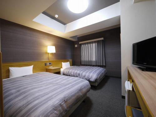 a hotel room with two beds and a flat screen tv at Hotel Route-Inn Yokote Inter in Yokote