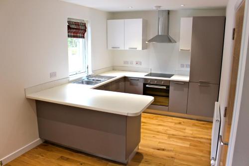 cocina con armarios blancos y encimera blanca en 2 Dellmhor Cottages, en Aviemore