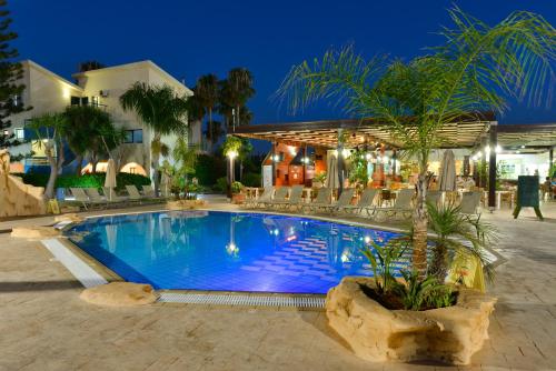 a swimming pool in front of a hotel at night at Makronisos Village in Ayia Napa