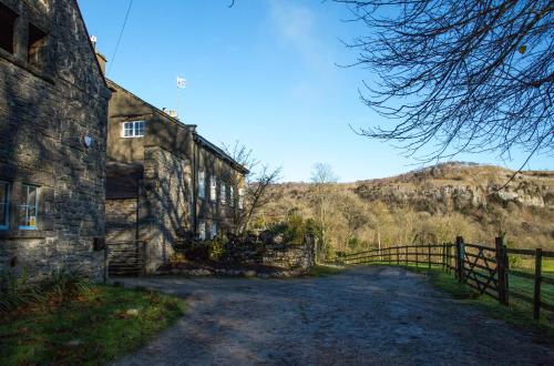 an old stone building with a fence on a dirt road at Witherslack Hall Farmhouse in Grange Over Sands