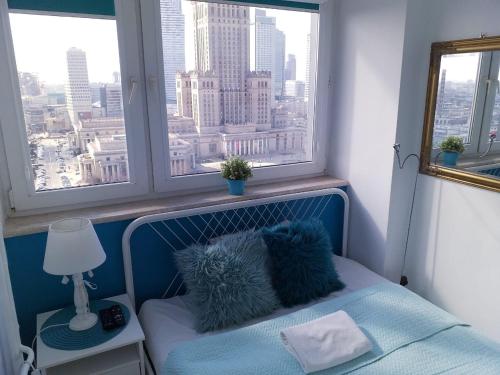 1 cama con 2 almohadas azules en una habitación con ventanas en Centre Apartamenty Warszawa, en Varsovia