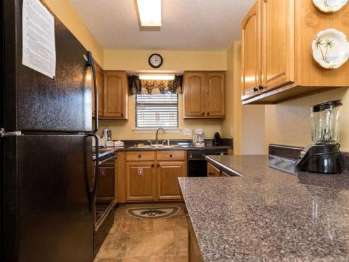 a kitchen with wooden cabinets and a black refrigerator at The Landing 203 by Meyer Vacation Rentals in Gulf Shores