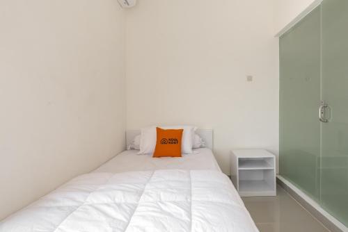 a bedroom with a white bed with an orange pillow on it at KoolKost near T2 Juanda Airport in Sidoarjo