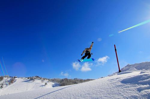 Ein Mann, der durch die Luft fliegt, während er auf einem Snowboard reitet. in der Unterkunft Hotel Silk Inn Madarao in Iiyama