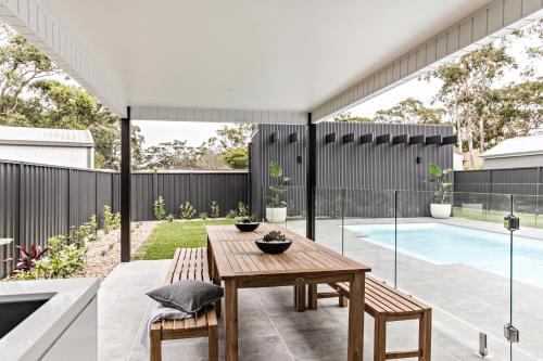 Un patio con mesa y sillas y una piscina. en Mandala Beach House Jervis Bay, en Callala Bay