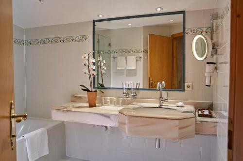 ein Badezimmer mit einem Waschbecken, einer Badewanne und einem Spiegel in der Unterkunft Hotel Erzberg in Zürs am Arlberg