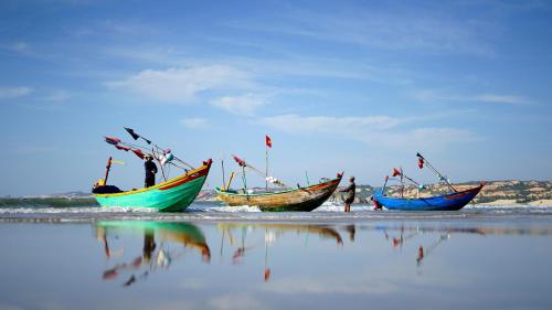 two boats on the beach with people in the water at Stop And Go Lang Chai Boutique Resort in Phan Thiet