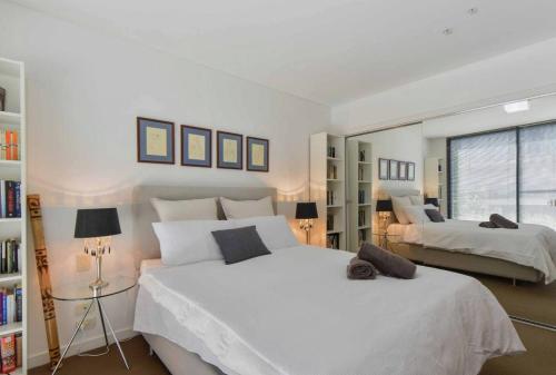 a white bedroom with two beds and a window at HAZEL Chapel St Socialite. Pool, Spa & Gym in Melbourne