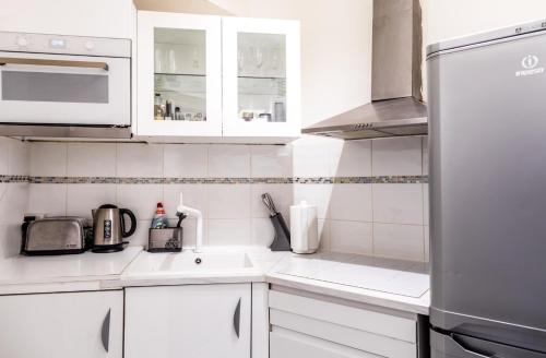 La cuisine blanche est équipée d'un évier et d'un réfrigérateur. dans l'établissement Flat 25 Dudley Court, à Londres