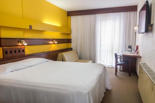 a hotel room with a white bed and a desk at Hotel Vinocap in Bento Gonçalves