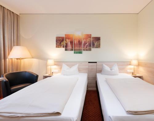 a hotel room with two beds and a chair at NOVINA HOTEL Südwestpark in Nürnberg