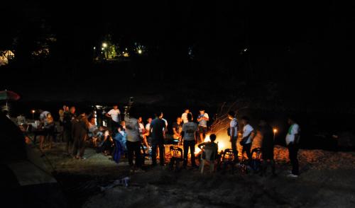 Un groupe de personnes debout autour d'un feu la nuit dans l'établissement Baantantara, à Suan Phueng