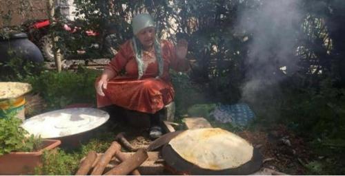 a woman sitting on the ground next to a grill at bedouin guest house in Rūmat Heib