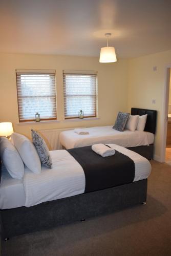 two beds in a room with two windows at Kelpies Serviced Apartments Kavanagh- 5 Bedrooms in Bathgate