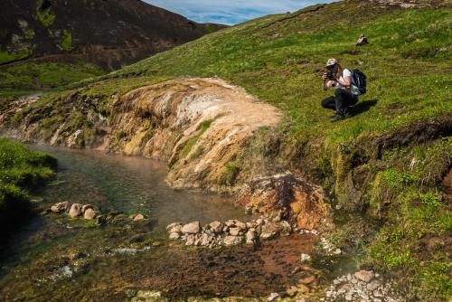 two people sitting on a hill next to a river at Reykjadalur Guesthouse in Hveragerði
