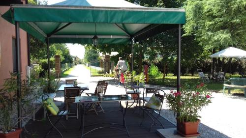 a patio with tables and chairs under a green canopy at Agriturismo Le oche selvatiche in Lauzacco