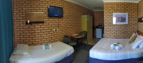 a room with two beds and a tv on a brick wall at Toukley Motel in Toukley