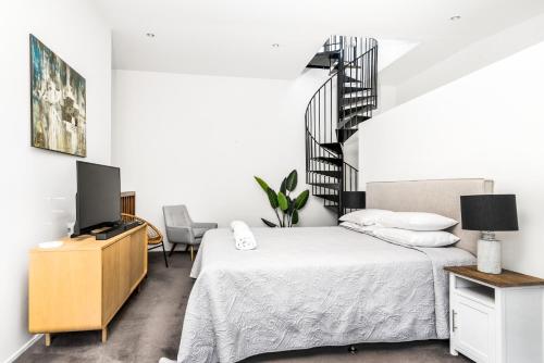 a bedroom with a bed and a tv and a staircase at Byron Butter Factory Apartments in Byron Bay
