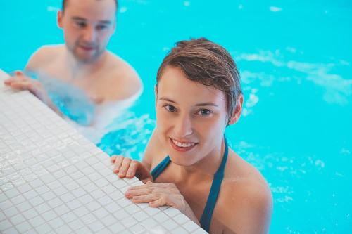 a man and woman in a swimming pool holding a surfboard at Pałac Brunów - Wellness & SPA in Lwówek Śląski